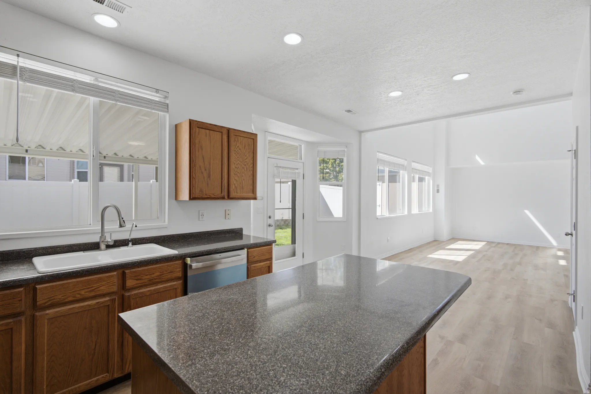 Kitchen featuring wood cabinetry, a white basin sink, stainless steel dishwasher, and dark countertop surfaces