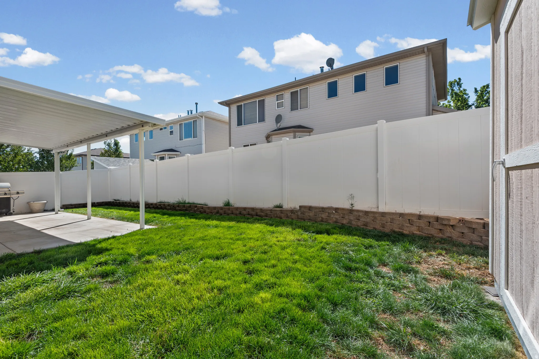 Spacious backyard featuring a covered patio, concrete slab, and a green lawn