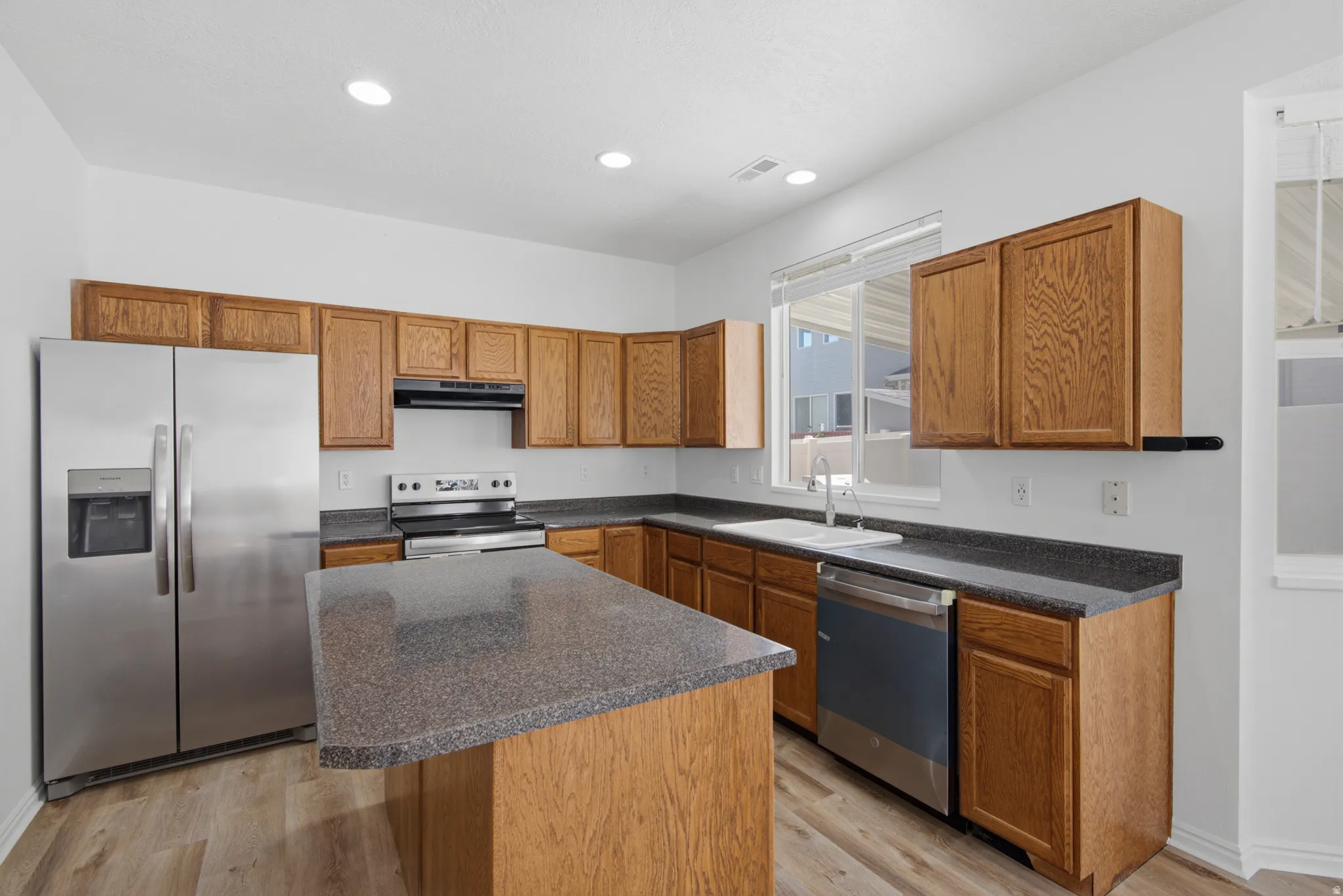 Kitchen with an island, wood-finish cabinetry, stainless steel appliances, and dark countertops