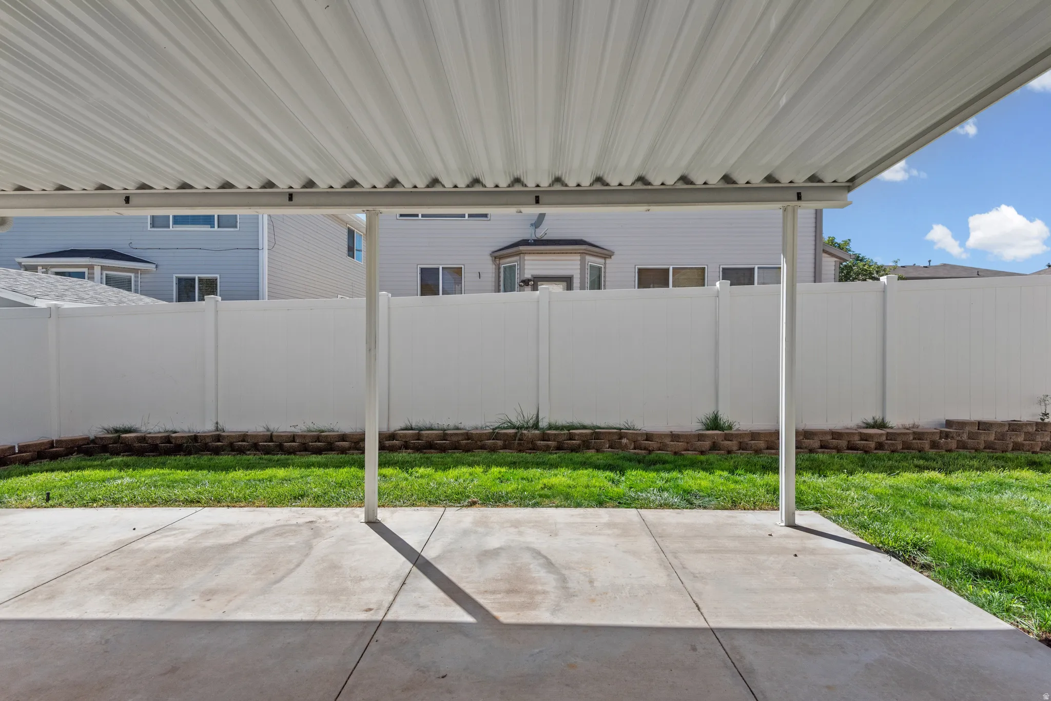 Expansive concrete patio with a full-coverage awning, surrounded by a vinyl privacy fence
