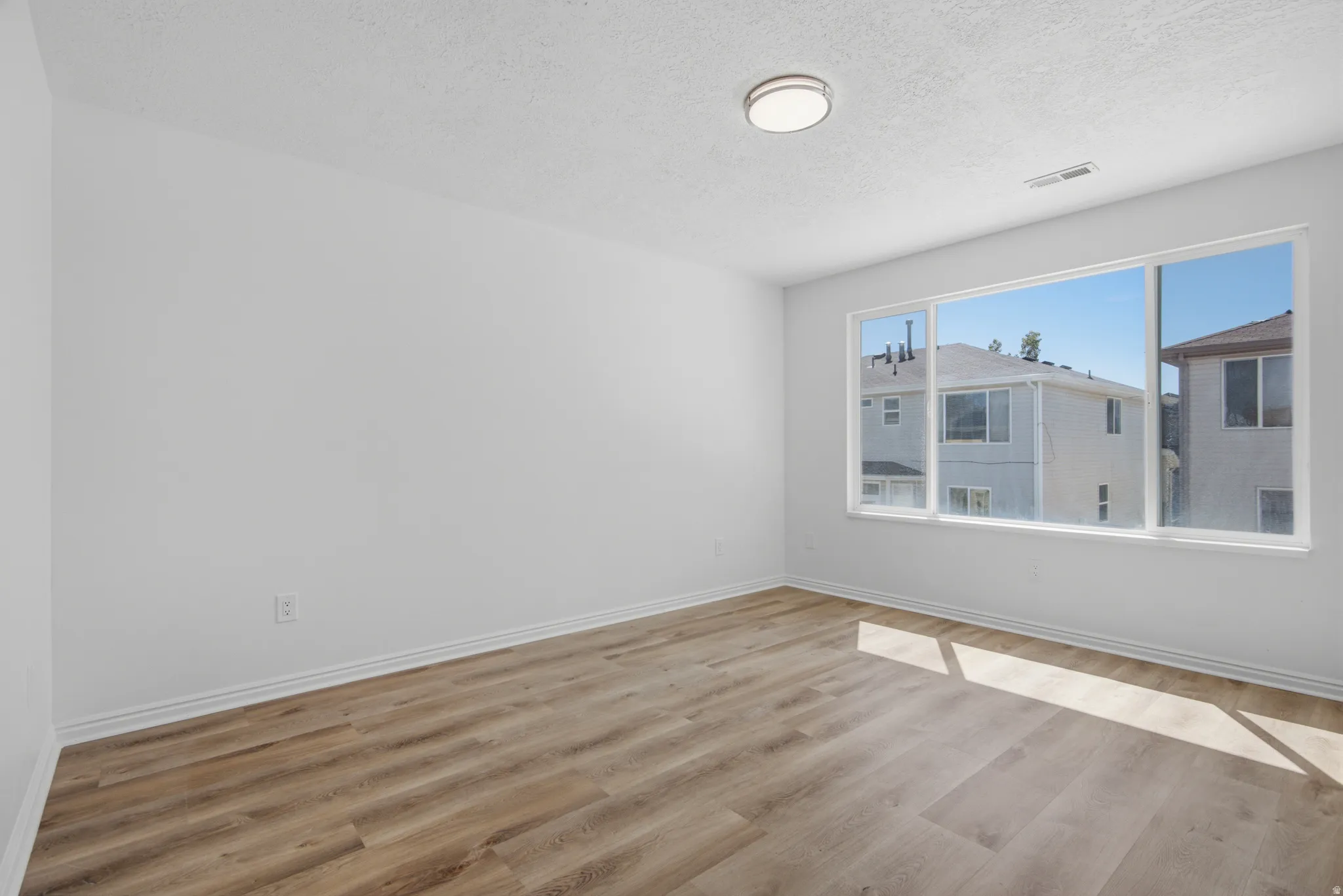 Expansive window offering abundant natural light, wood-finish flooring, recessed ceiling light fixture, and white wall finishes