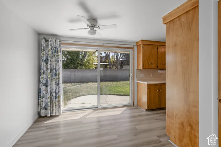 Wood-finish flooring, sliding glass door to the backyard, ceiling fan with light fixture, and wood cabinetry with countertops
