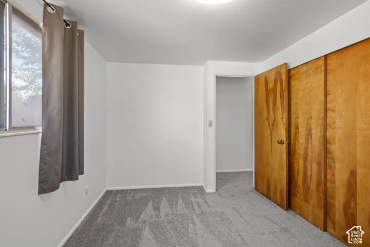 Window with natural light, neutral wall colors, wood-panel closet doors, and patterned carpet flooring