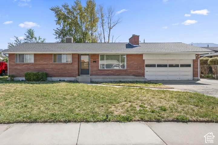 Brick exterior with an attached garage, paved driveway, and established landscaping