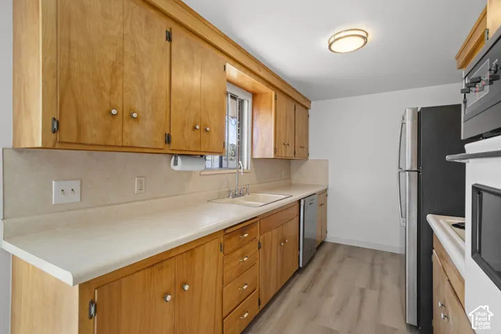 Kitchen with wood cabinetry, light-toned countertops, a stainless steel dishwasher, a black and stainless steel refrigerator, and wood-finish flooring