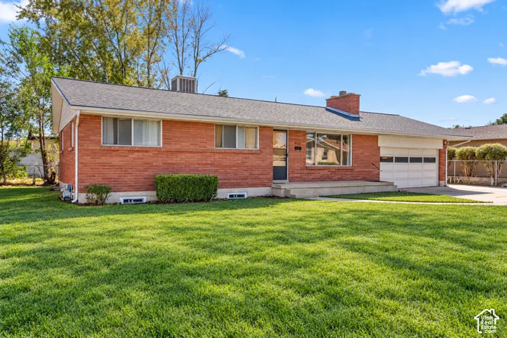 Single-story brick exterior featuring a multi-pane garage door, chimney, concrete porch, and expansive lawn