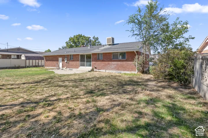 Rear brick exterior, concrete patio, sliding glass door, multiple windows, and a fenced yard