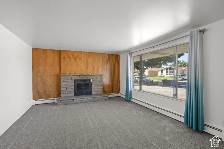 Spacious room featuring carpeting, a prominent fireplace with a stone hearth, and a wood-paneled accent wall