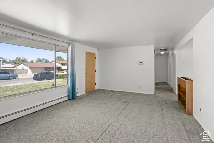 Expansive picture window, light gray carpeting, neutral wall paint, wood-finish interior door, and built-in shelving
