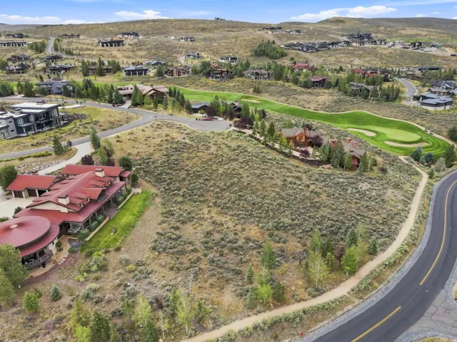 Expansive property with a paved road, natural landscaping, and a manicured golf course within the community