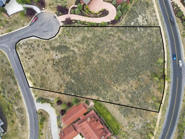 Expansive undeveloped lot featuring natural vegetation, bordered by paved roads, with surrounding residential development