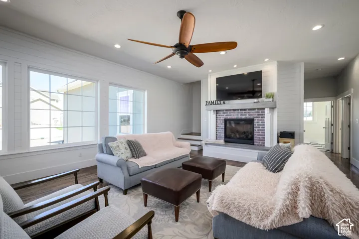 Spacious living area featuring large grid-pattern windows, a ceiling fan with wood-finish blades, recessed lighting, a fireplace with a brick surround, and a substantial mantel