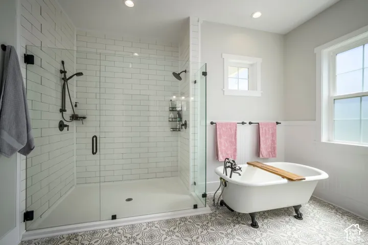 Glass-enclosed shower with subway tile surround, clawfoot tub, patterned floor tile, and dual windows