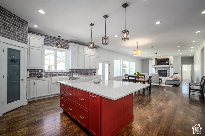 Open-concept living space with dark wood-finish flooring, white cabinetry, and a red kitchen island with a light-colored countertop