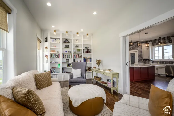 Built-in shelving with integrated lighting, recessed ceiling lights, wood-finish flooring, sliding barn door, and a kitchen with dark brick-style accent wall