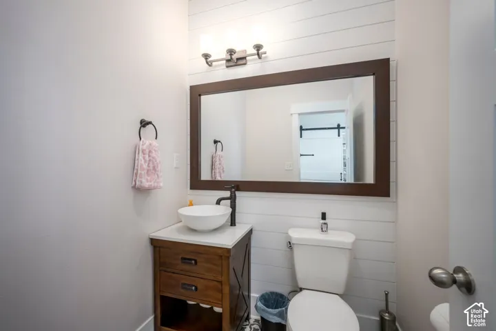 Shiplap accent wall, wood-finish vanity with drawer storage, white vessel sink, dark-toned faucet, and a wall-mounted light fixture