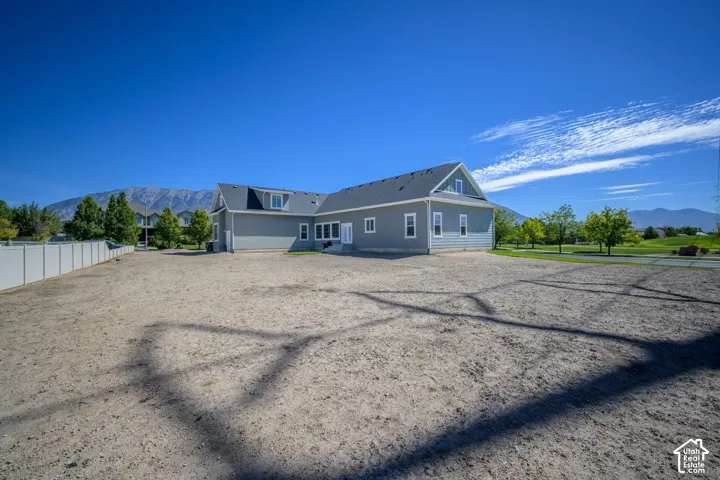 Expansive undeveloped yard space, light grey siding with white trim, dormer window, mountain backdrop, and a white fence