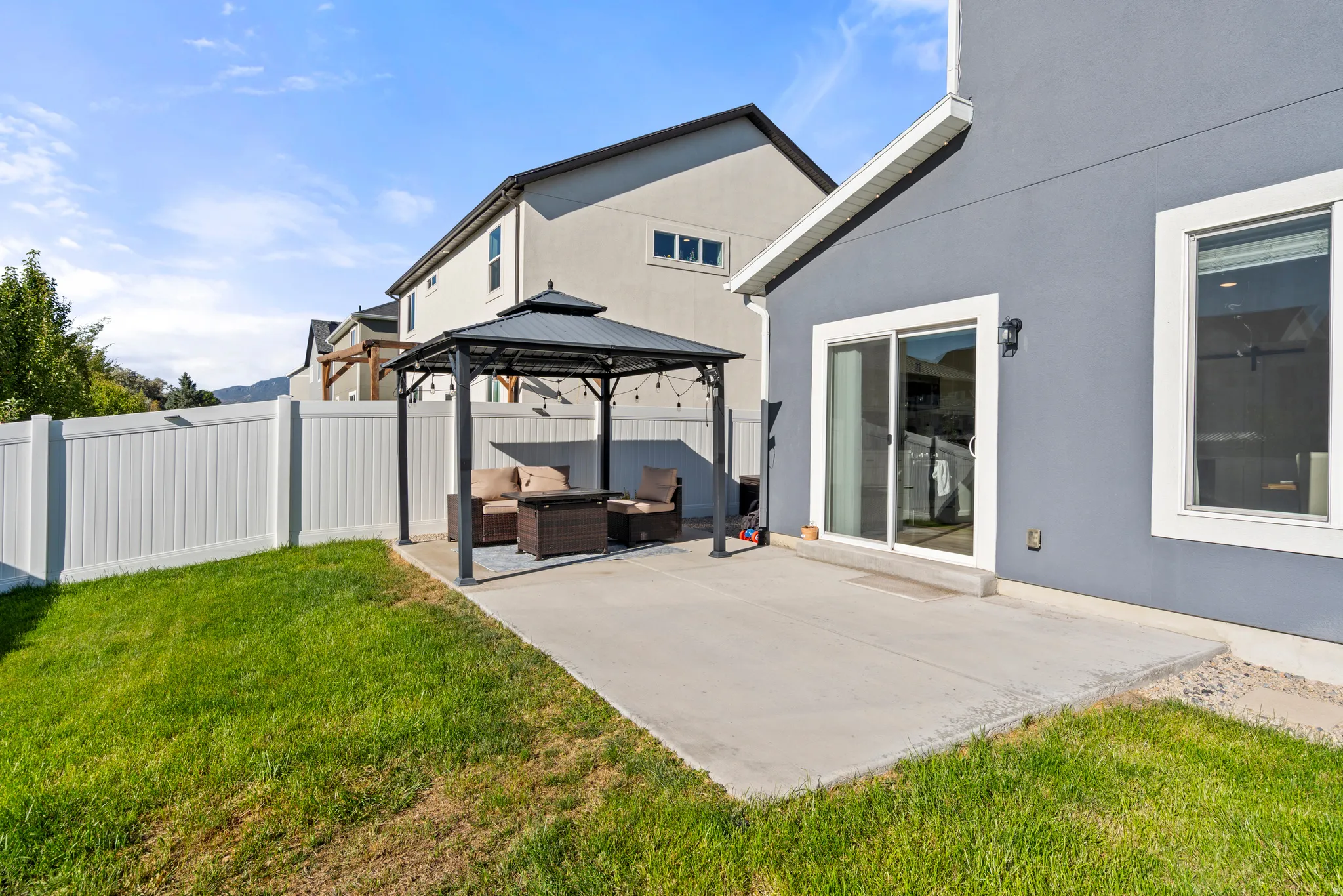 Concrete patio with sliding glass door access, enclosed by a white privacy fence