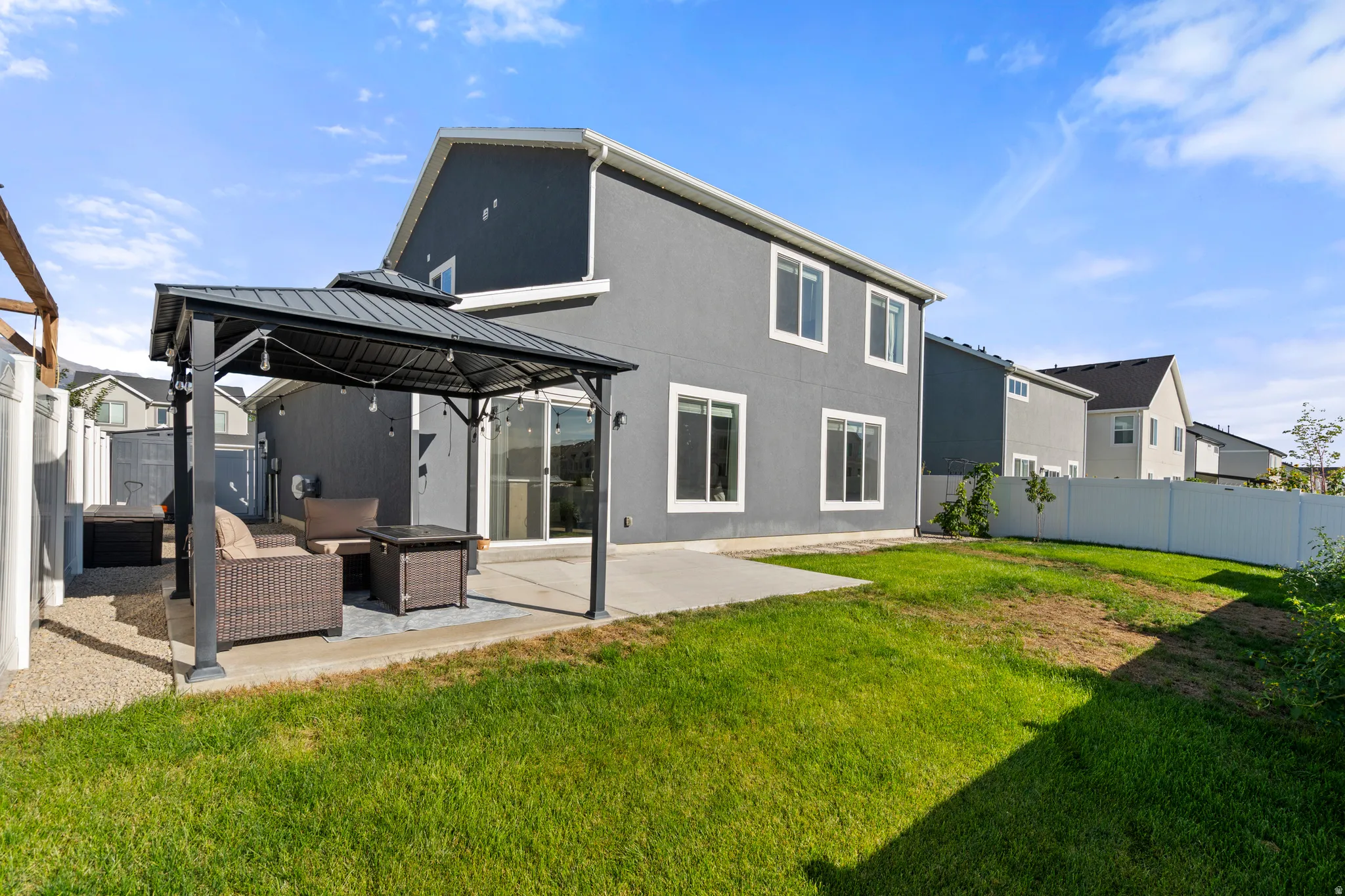 Rear exterior with gray stucco siding, white window trim, and a white privacy fence