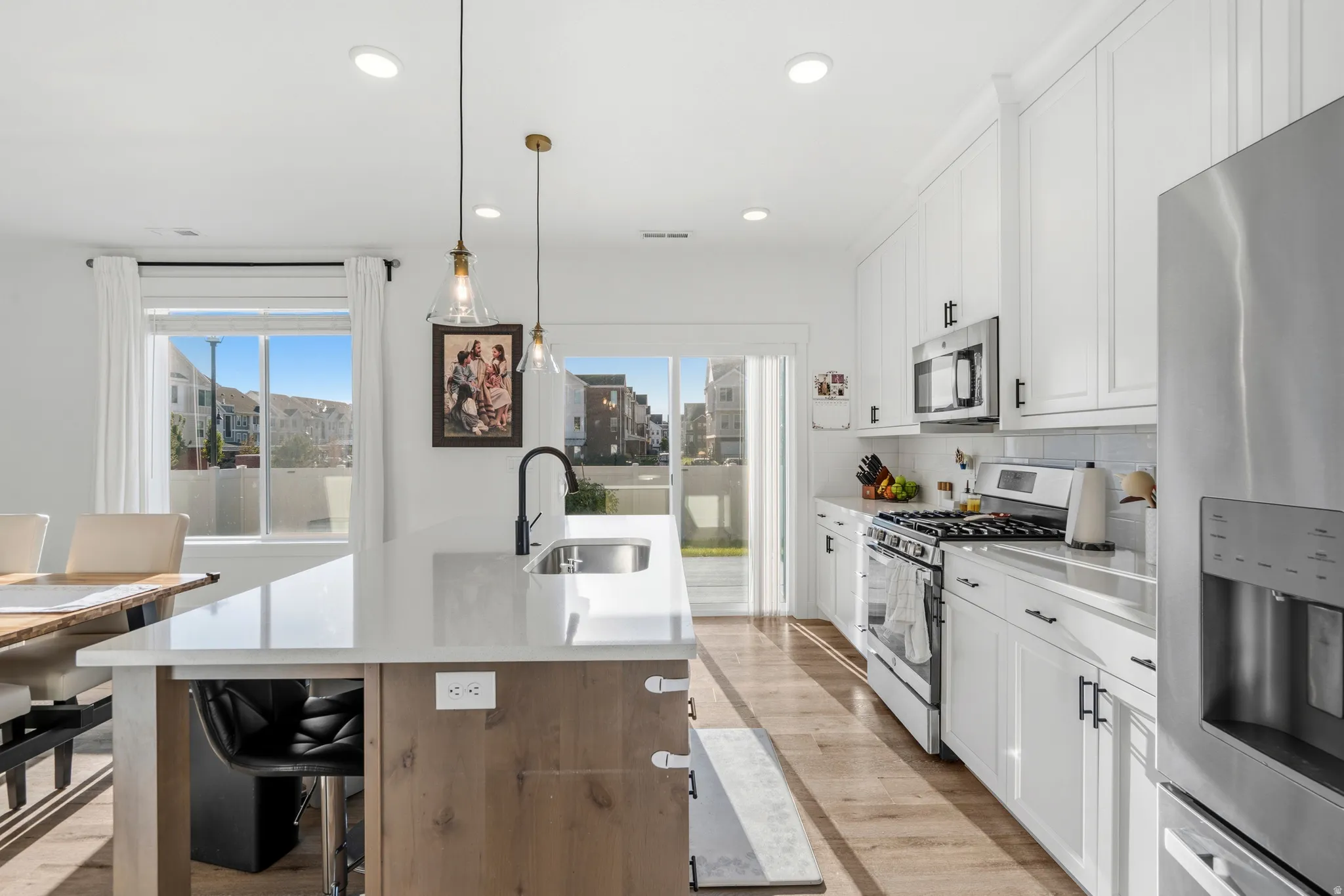 Modern kitchen featuring white cabinetry, stainless steel appliances, a center island with a sink, wood-finish flooring, and pendant lighting