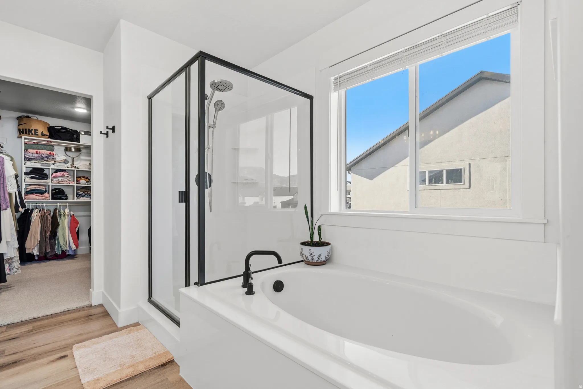 Soaking tub with a matte black faucet, glass-enclosed shower with black trim, and wood-finish flooring