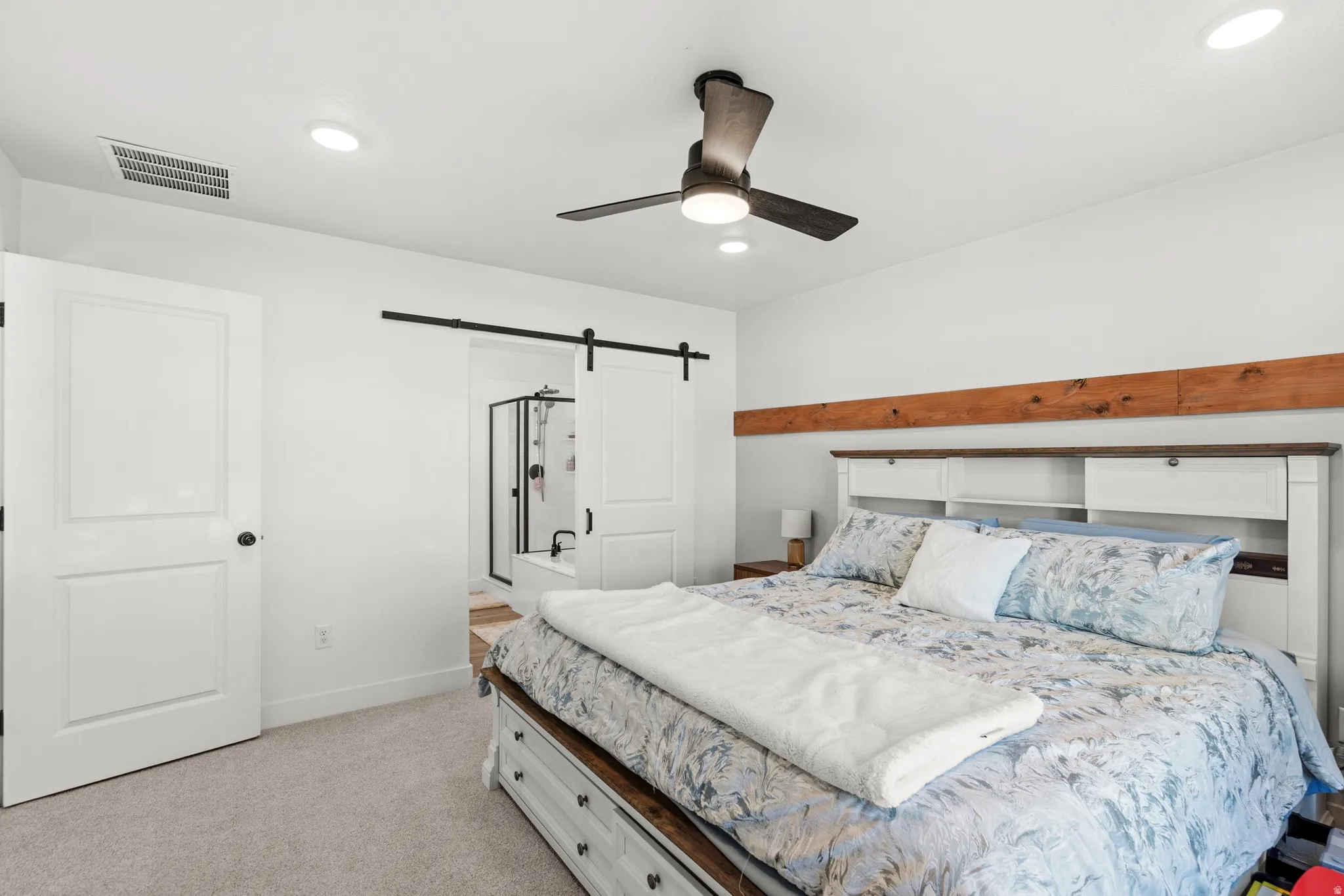 Recessed ceiling lighting, ceiling fan, natural wood beam accent, barn door entry to bathroom, and carpet flooring