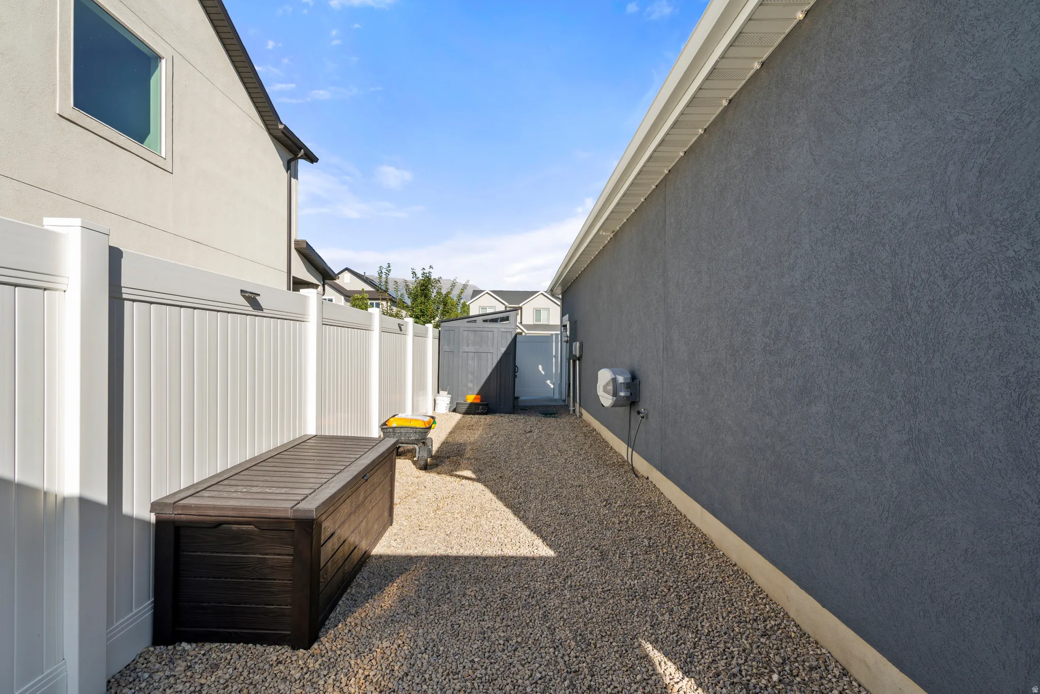 Gravel pathway bordered by a white vinyl privacy fence and a stucco exterior wall