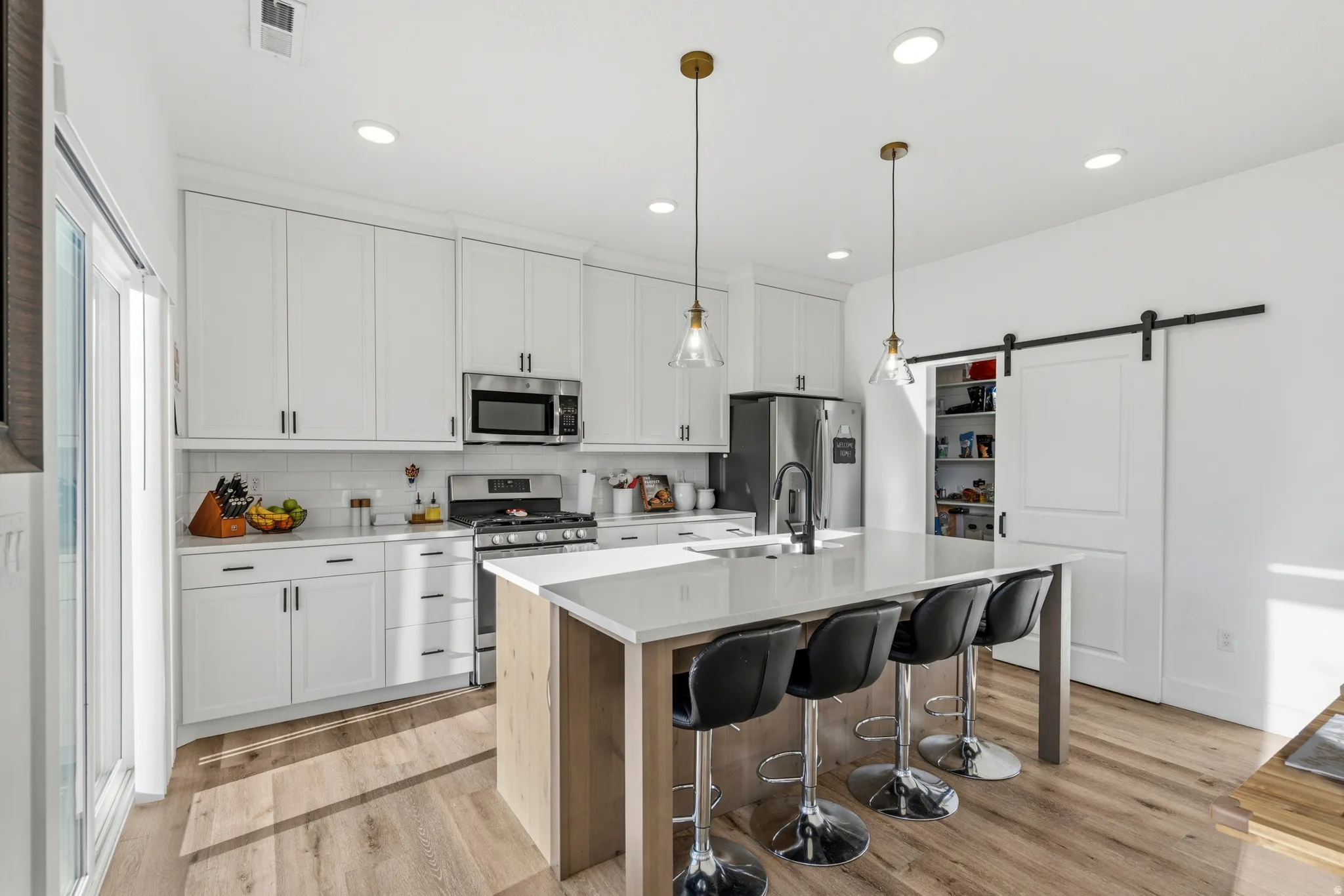 Kitchen featuring white shaker cabinetry, stainless steel appliances, a center island with countertop seating, wood-finish flooring, and a sliding barn door pantry