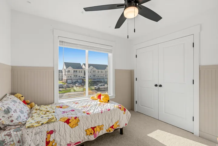 Wall-to-wall carpeting, white paneled double doors, horizontal window with blinds, beadboard wall paneling, and a ceiling fan with integrated lighting