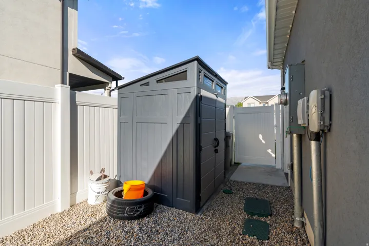Gravel pathway featuring a freestanding shed with integrated windows, a white privacy fence, and a concrete slab