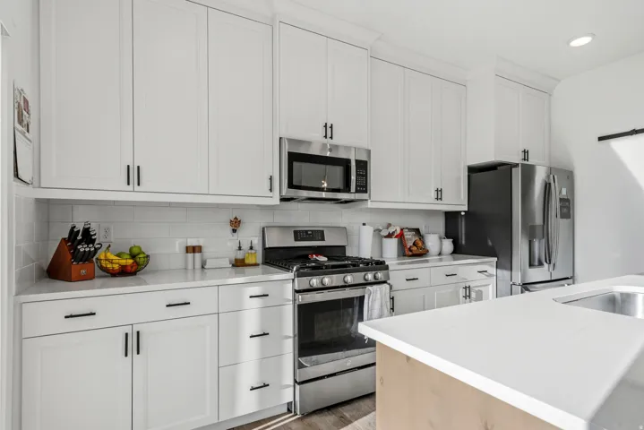 Bright kitchen featuring white shaker-style cabinetry, stainless steel appliances, a subway tile backsplash, and light-toned countertops