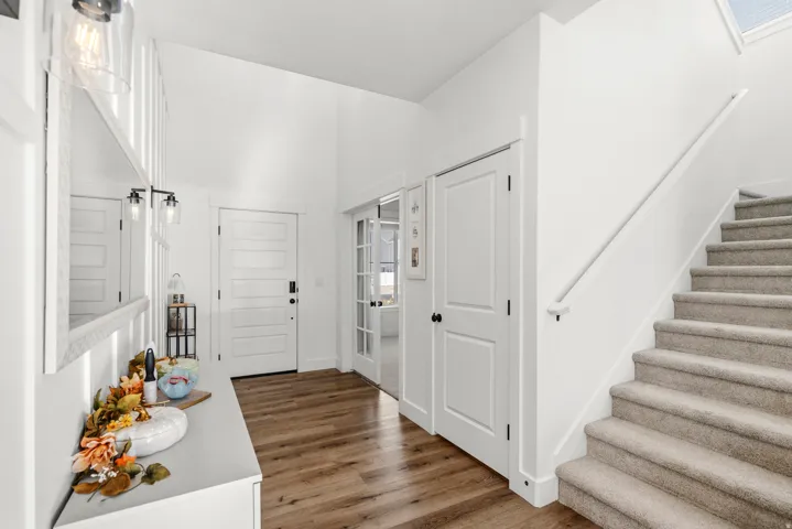 Vaulted entry with wood-finish flooring, white paneled doors, and a carpeted staircase with a skylight
