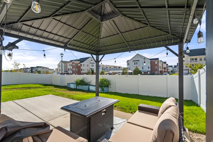 Concrete patio with a metal gazebo, string lighting, and a white privacy fence