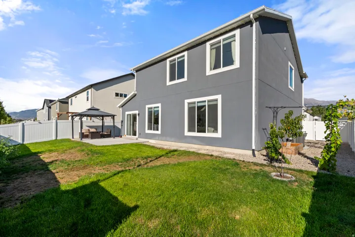 Expansive backyard with a manicured lawn, white privacy fencing, and a concrete patio featuring a gazebo