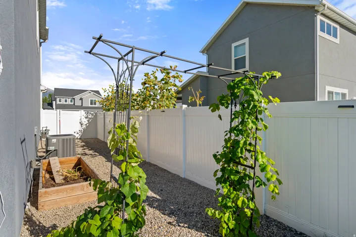 Enclosed side yard featuring a white privacy fence, gravel pathway, and a metal arbor with climbing plants