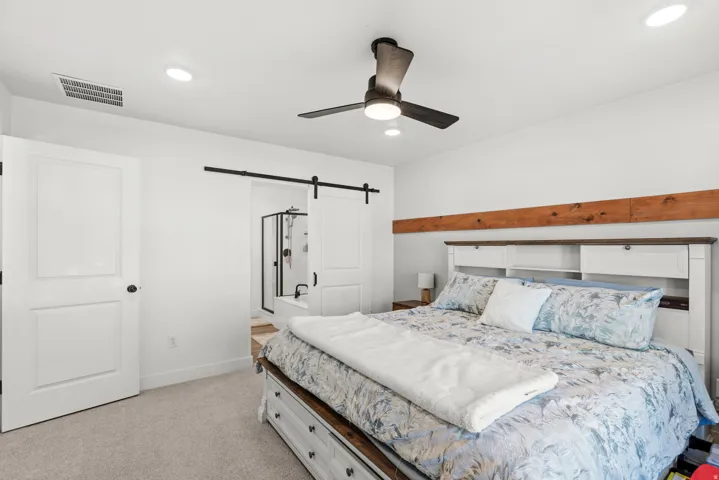 Recessed ceiling lighting, ceiling fan, natural wood beam accent, barn door entry to bathroom, and carpet flooring
