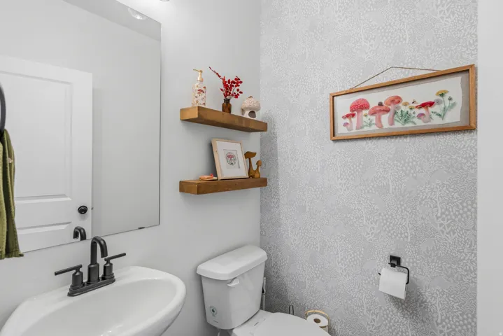 Pedestal sink with a matte black faucet, wall-mounted mirror, and two wooden floating shelves