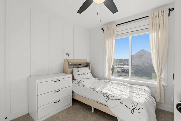 Vertical wall paneling, large window with natural light, ceiling fan, and carpeted flooring