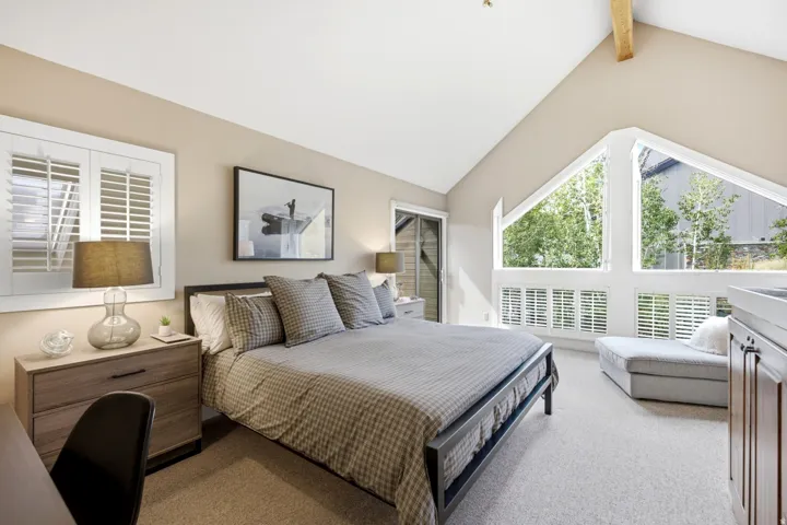 Primary Suite offers vaulted ceiling with exposed wood beam, large triangular windows with plantation shutters, wood-finish built-in cabinetry and private balcony.