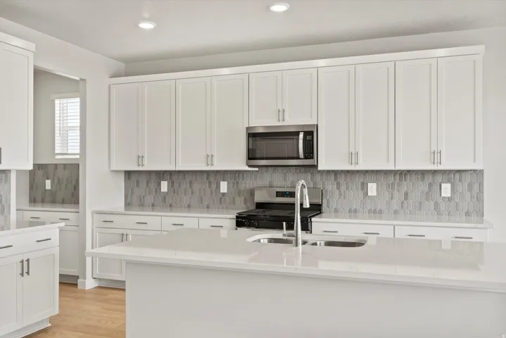 White shaker cabinetry with brushed nickel hardware, light-toned countertops, geometric tile backsplash, stainless steel microwave, and wood-finish flooring
