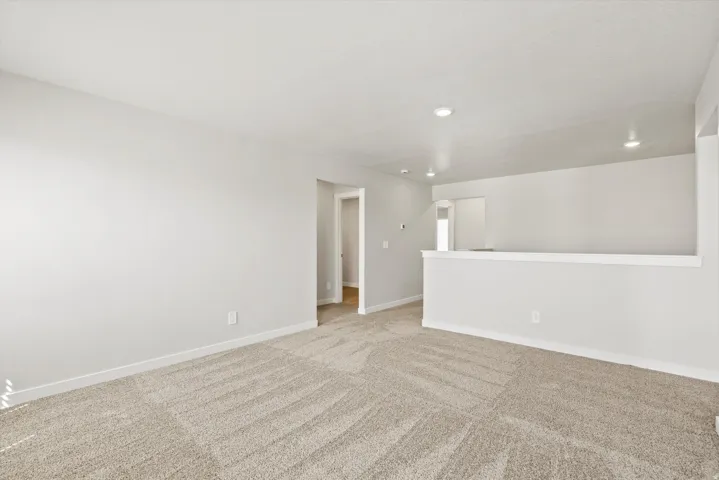 Neutral color palette, recessed lighting, light-toned carpeting, white trim, and a partial wall separation