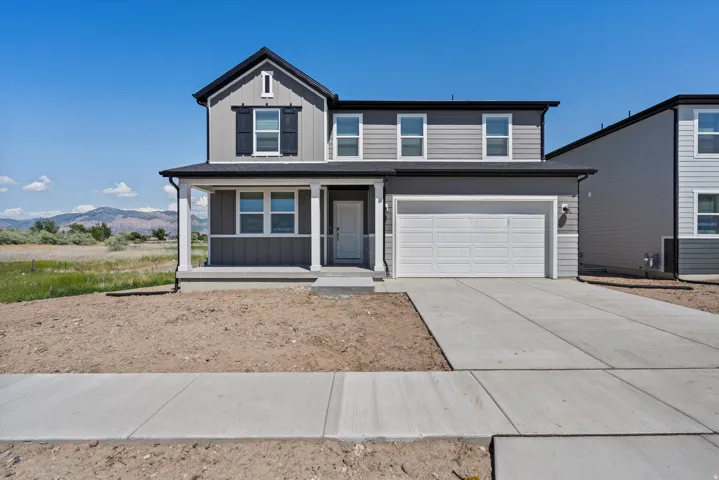 Two-story residence featuring a covered front porch, attached two-car garage, concrete driveway, and a light gray exterior with dark shutters