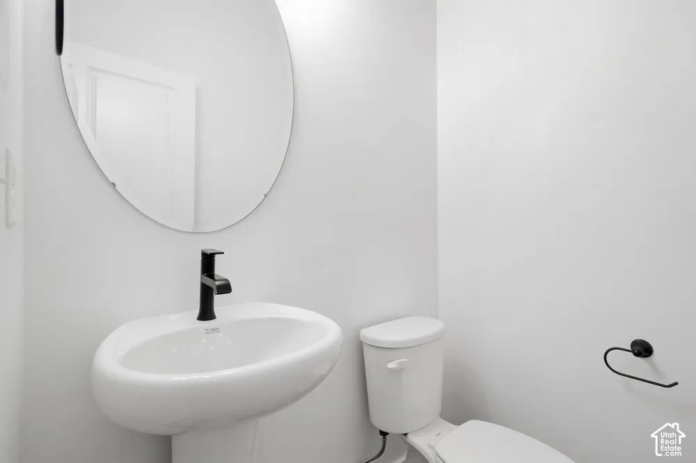 Oval wall-mounted mirror, white pedestal sink, matte black faucet, and matte black hardware