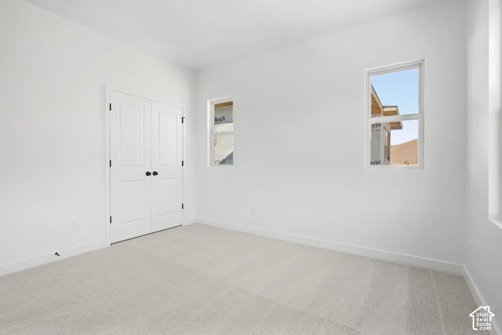 Neutral-toned carpeted flooring, white walls, and double doors featuring matte black hardware, accompanied by two windows