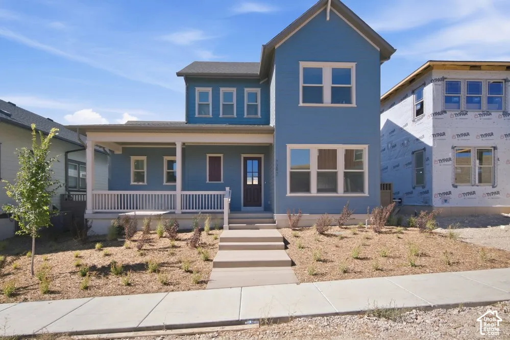 Two-story exterior featuring blue siding, a covered front porch with white railing, and multi-light windows