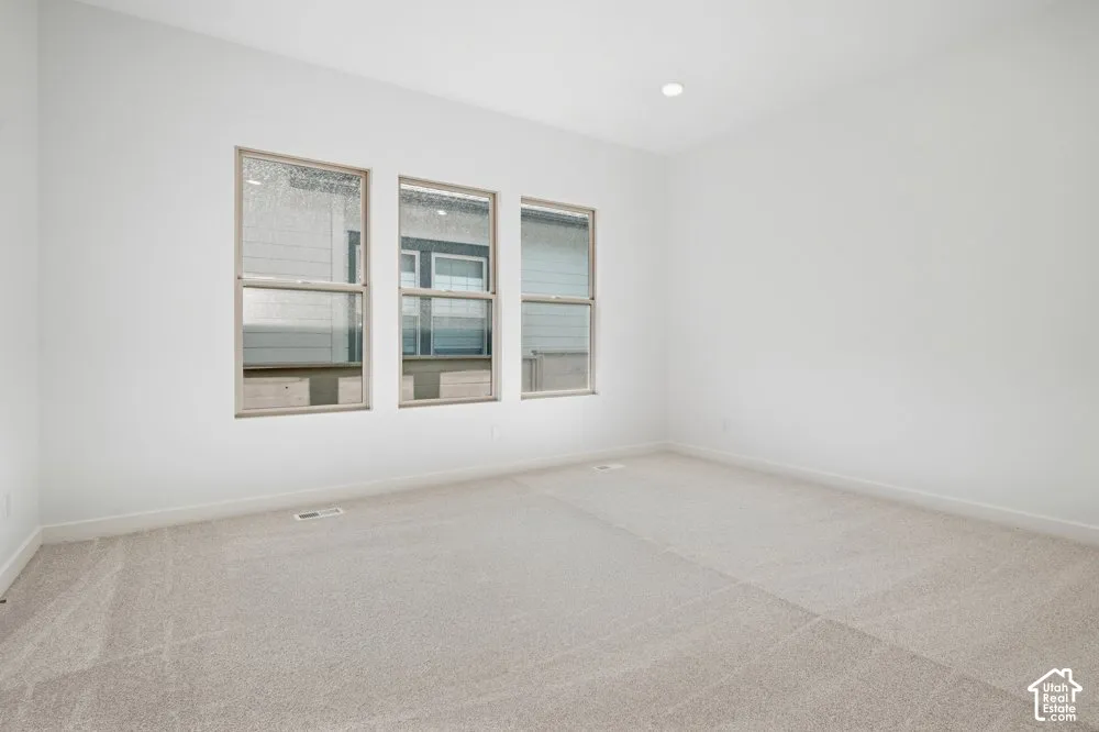 Neutral-toned carpeting, high ceilings with recessed lighting, and a triple-window configuration with frames