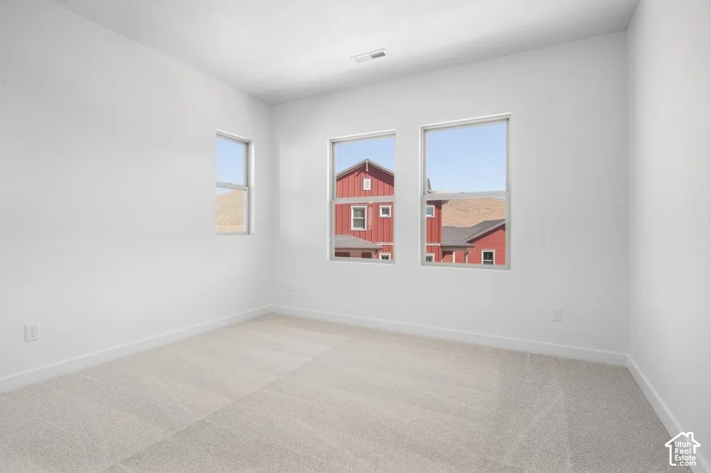 Neutral-toned interior space featuring light-colored wall-to-wall carpeting, crisp white walls, and triple window configuration