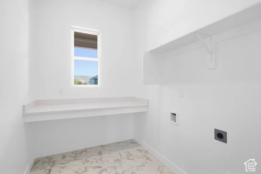 Laundry area featuring light-toned stone-patterned flooring, a built-in countertop, an upper storage shelf, and a window