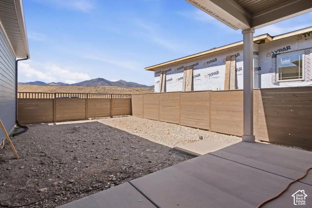 Covered concrete patio with horizontal wood-style fencing, gravel landscaping, and mountain backdrop