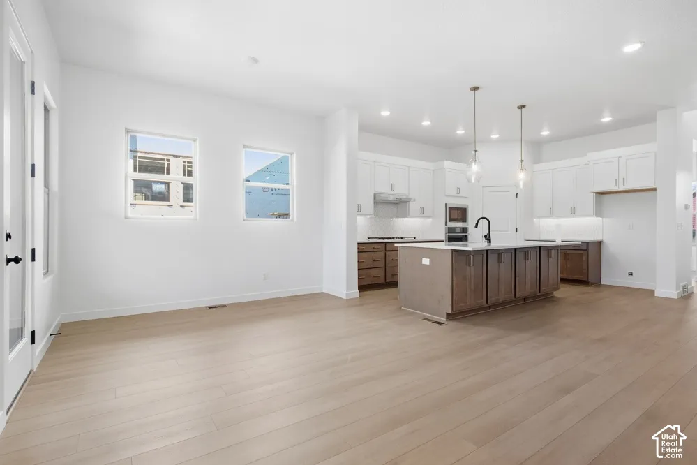 Open-concept kitchen featuring two-tone cabinetry, a central island with stone-finish countertops, wood-finish flooring, and recessed lighting